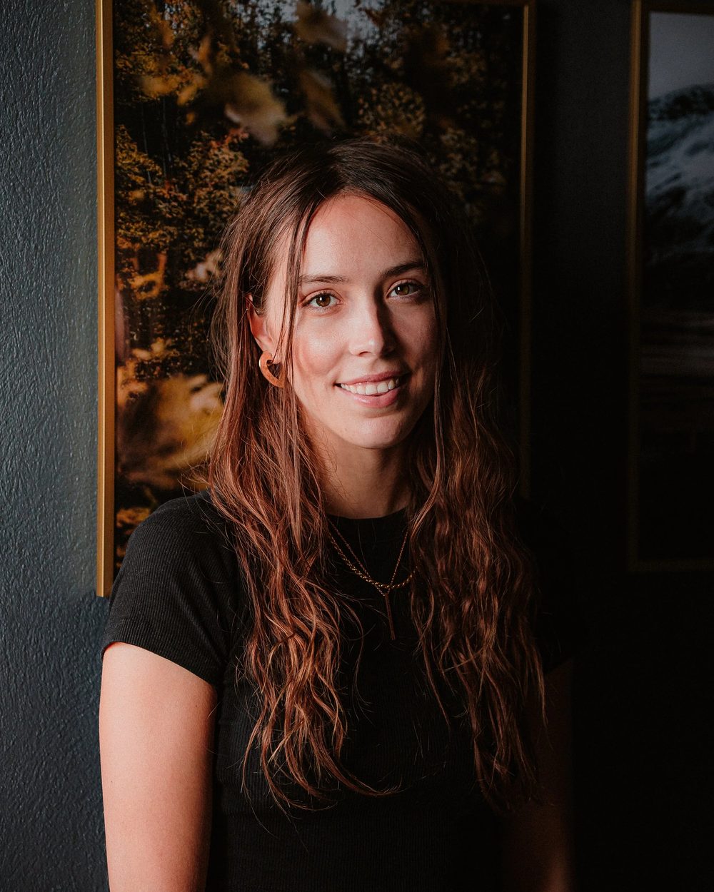 Käti, smiling, in front of framed nature photographs on a dark wall.